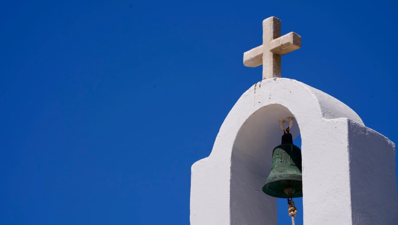 Clocher blanchi à la chaux avec sa cloche en bronze et une croix de pierre, sur un ciel bleu intense