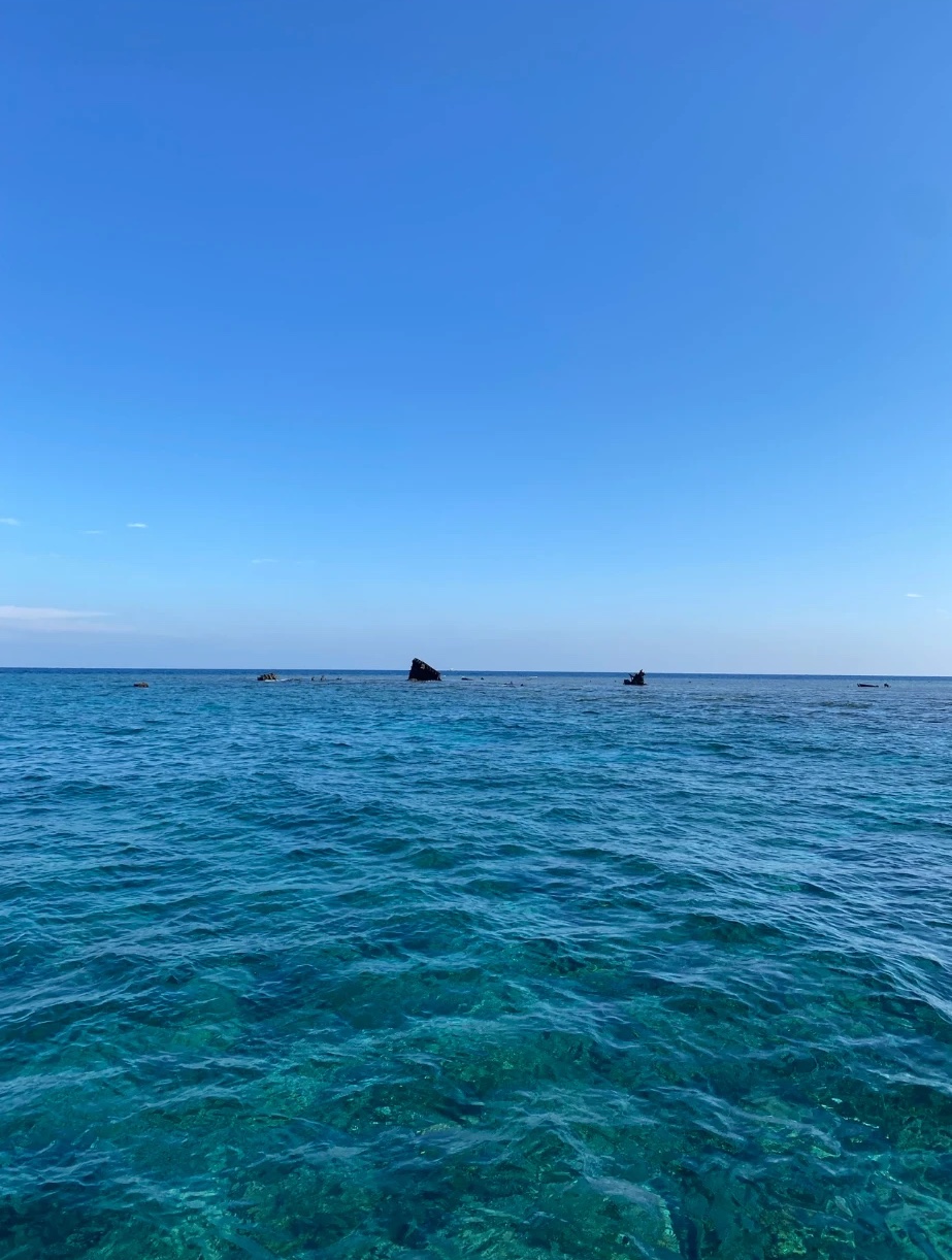 Mer turquoise et transparente, une épave affleure à l'horizon sous un ciel bleu