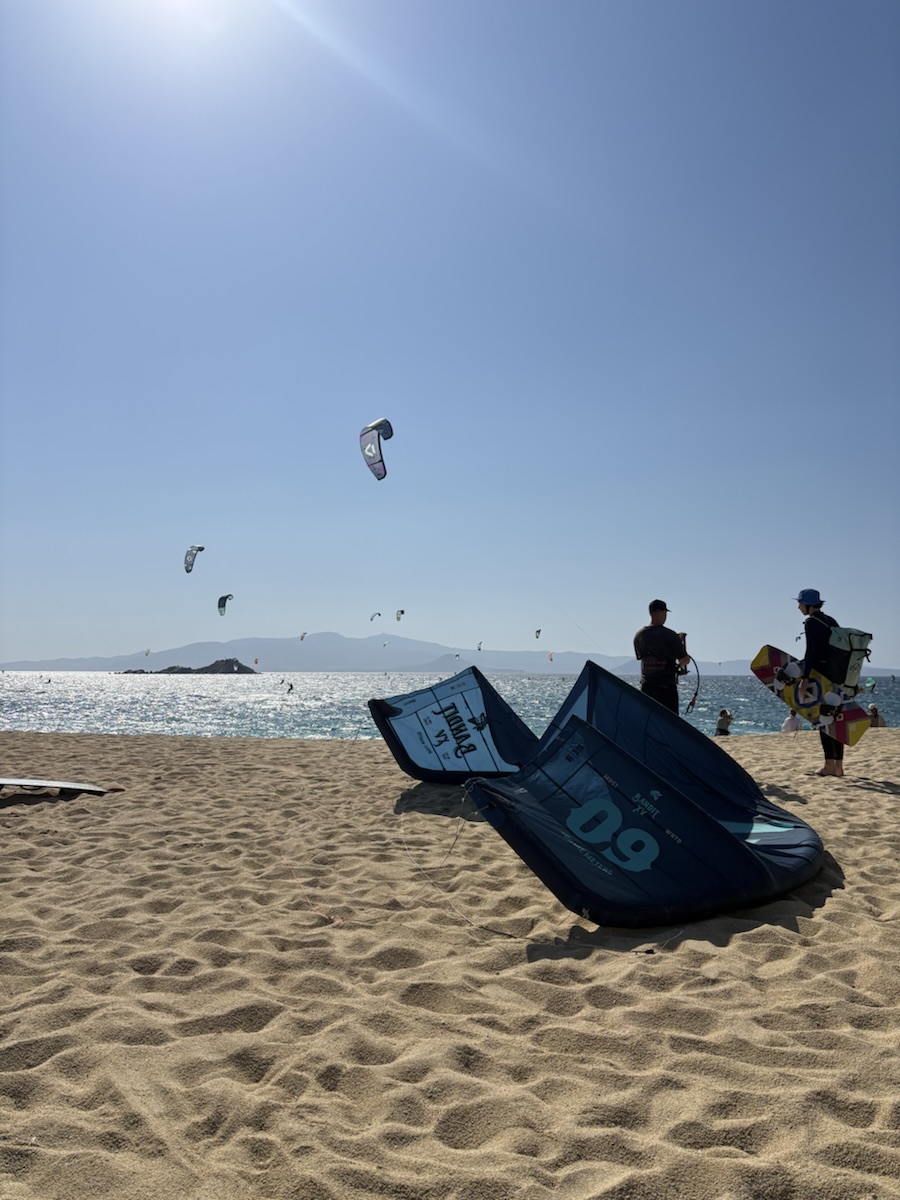 Ailes de kitesurf posées sur le sable, d'autres kites dans le ciel au-dessus de la mer